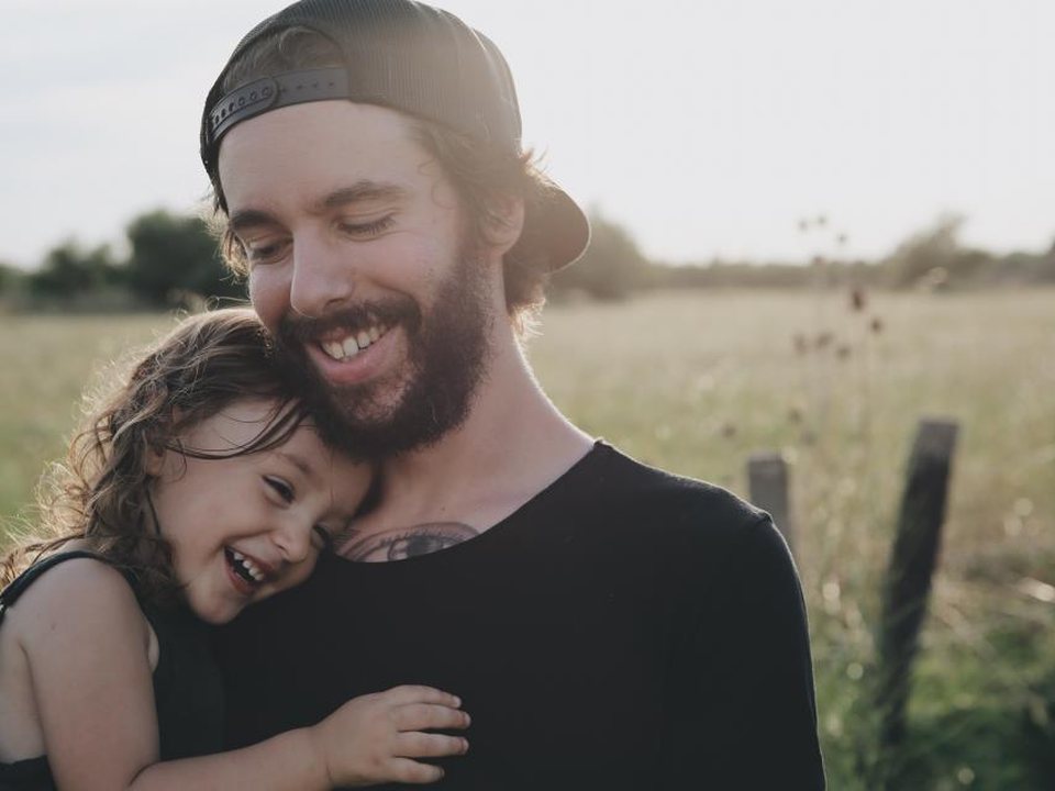 Papà sorridente abbraccia la figlia in un campo al tramonto