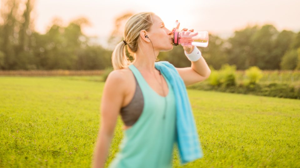 Donna beve acqua dopo l'attività fisica in un parco